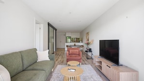 Ein modernes Wohnzimmer mit einem grünen Sofa, einem roten Sessel, einem Couchtisch, einem Fernseher und einer Küche im Hintergrund.