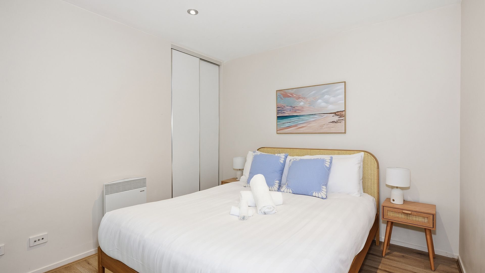 Ein Schlafzimmer mit Bett, Nachttisch, Lampe, Gemälde und Kleiderschrank.