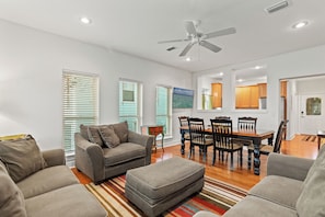 A spacious living room with a gray sofa, ottoman, dining table with chairs, and a ceiling fan. - Stay at The Hut! Room for everyone! 4BR Fun Sleeps 11 (Santa Rosa Beach)