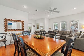 A spacious living room with a dining area, a ceiling fan, and a large mirror. - Stay at The Hut! Room for everyone! 4BR Fun Sleeps 11 (Santa Rosa Beach)