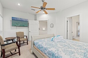 A bedroom with a bed, a chair, a ceiling fan, a painting, and a door leading to another room. - Stay at The Hut! Room for everyone! 4BR Fun Sleeps 11 (Santa Rosa Beach)