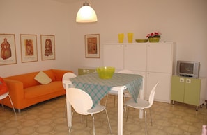 A dining area with a table, chairs, a sofa, a cabinet, and a television. - Villa With a Large Fenced Garden (Lignano Sabbiadoro)