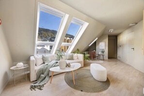 Um loft moderno com teto inclinado, grandes janelas, sofá, mesa de centro e pequena área de refeições.