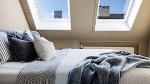 Una camera da letto con un letto, cuscini, una coperta e due lucernari.