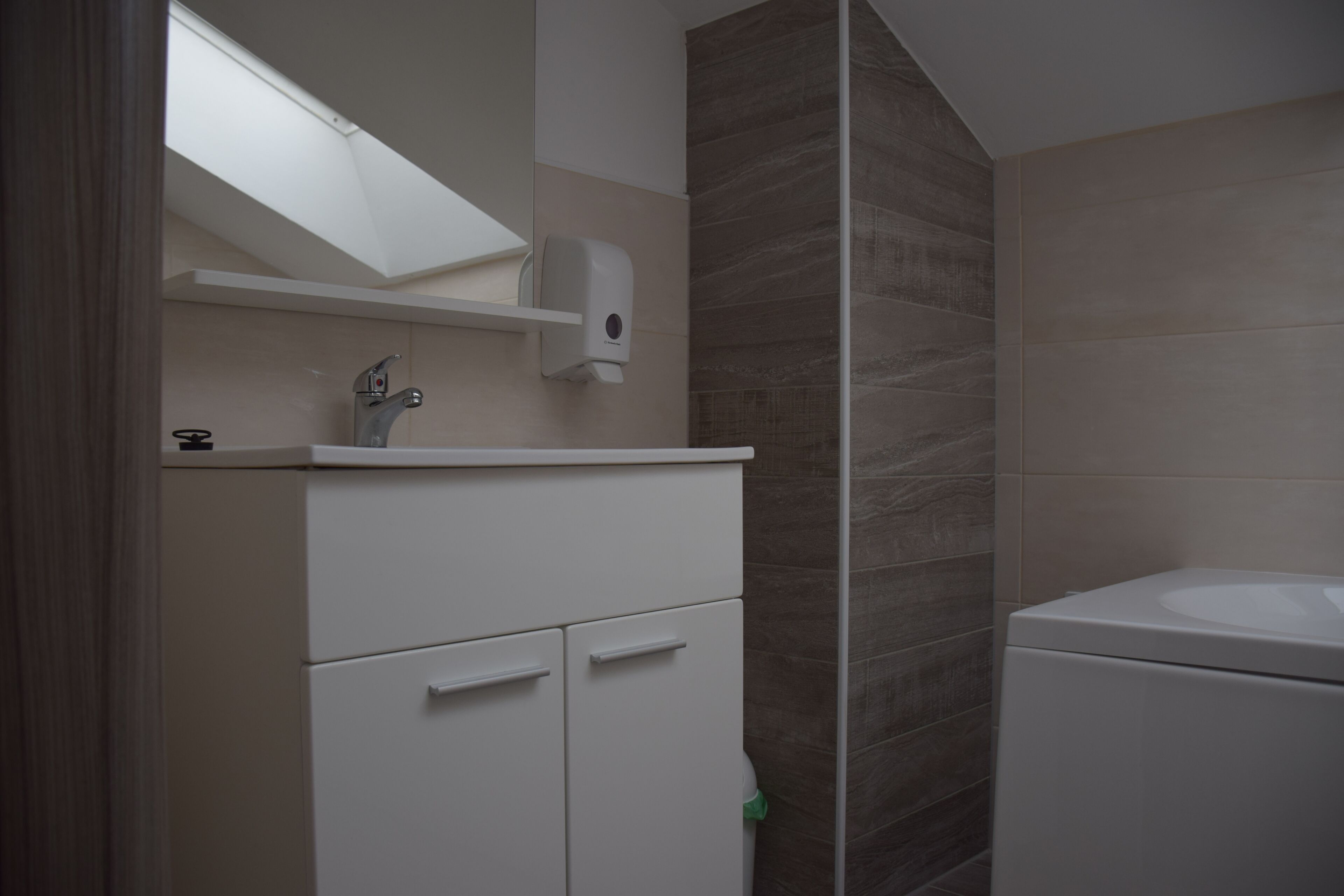 A bathroom with a sink, a mirror, a soap dispenser, and a toilet.