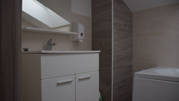 A bathroom with a sink, a mirror, a soap dispenser, and a toilet.