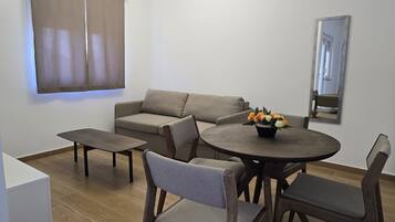 Een woonkamer met een bank, een ronde tafel met stoelen, een bijzettafeltje en een bloevas.