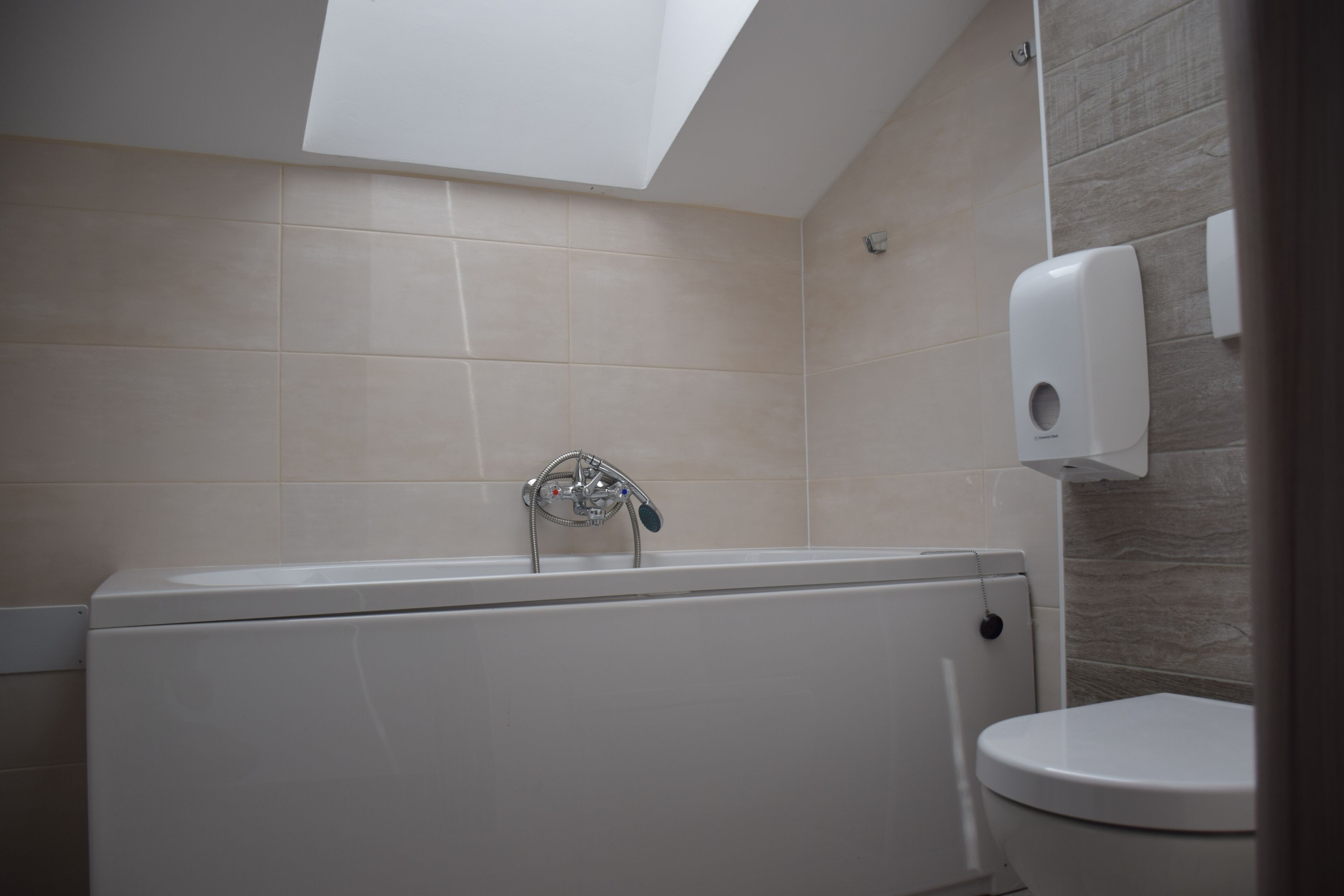Een badkamer met een dakraam, een bad, een toilet en een zeepdispenser.