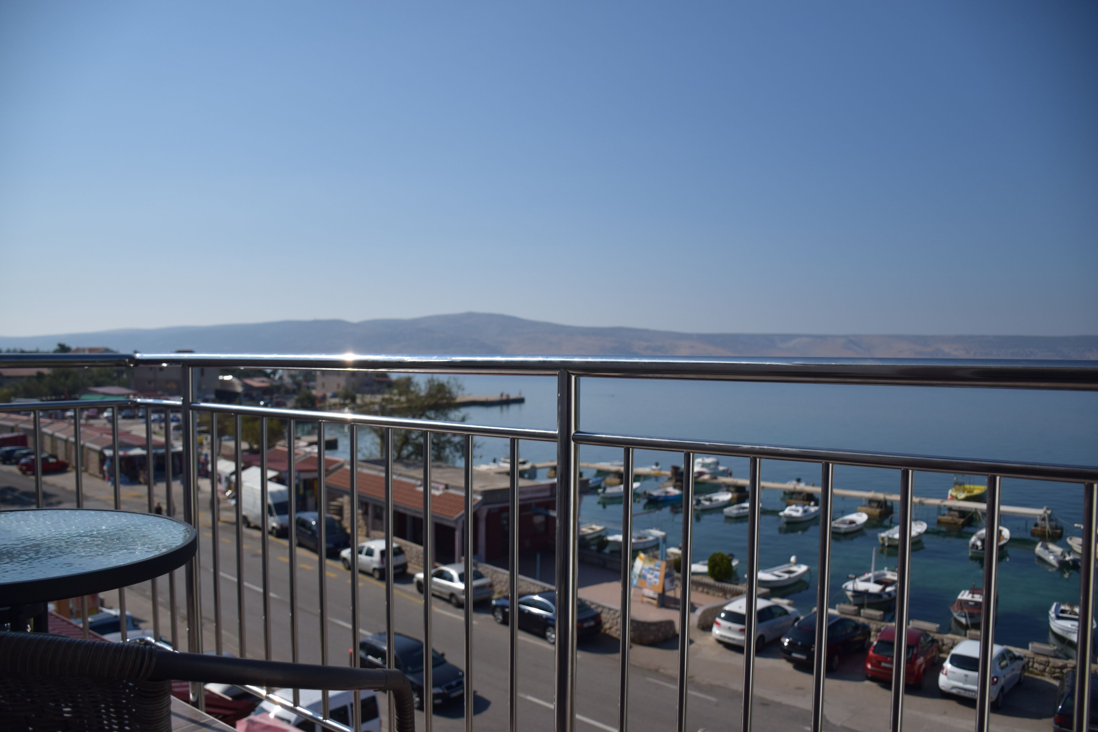 A balcony with a view of a marina, parked cars, and distant mountains.