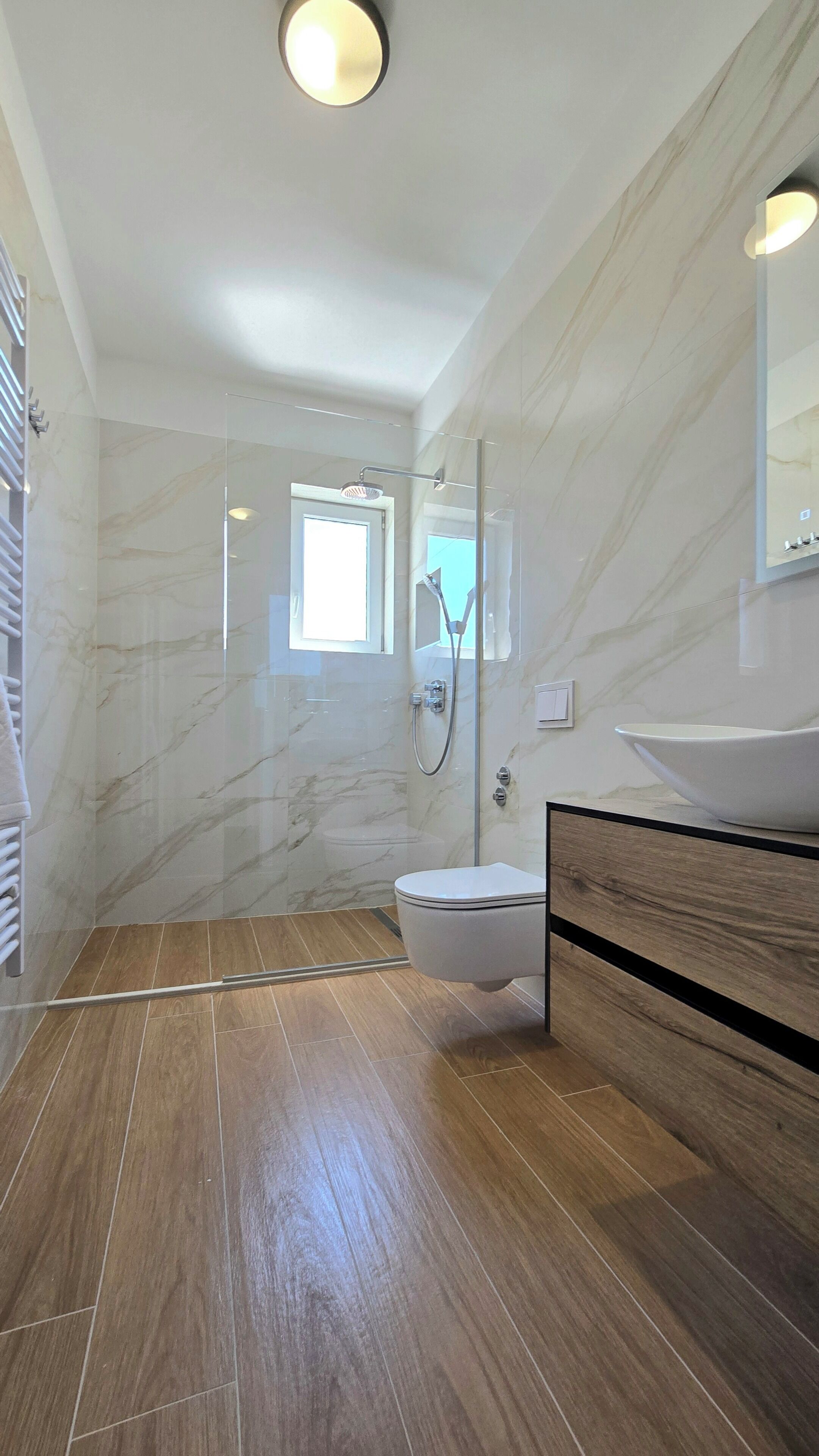 Een badkamer met een douchecabine, toilet, wastafel met spiegel en een raam voor natuurlijk licht.