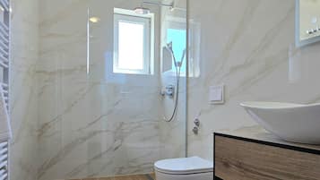 Een badkamer met een douchecabine, toilet, wastafel met spiegel en een raam voor natuurlijk licht.