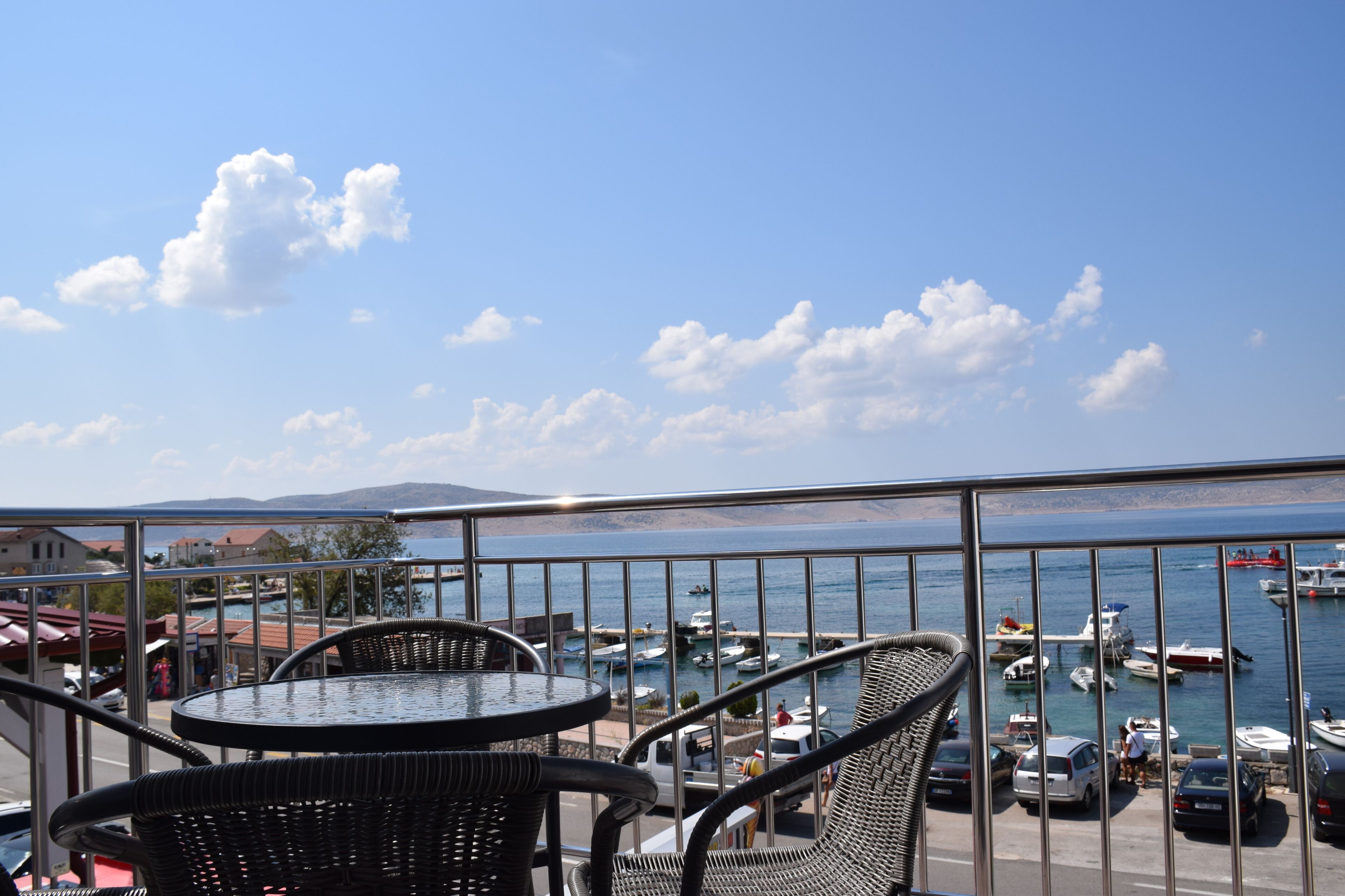 A balcony with wicker chairs and a table overlooking a marina with boats and a clear sky.