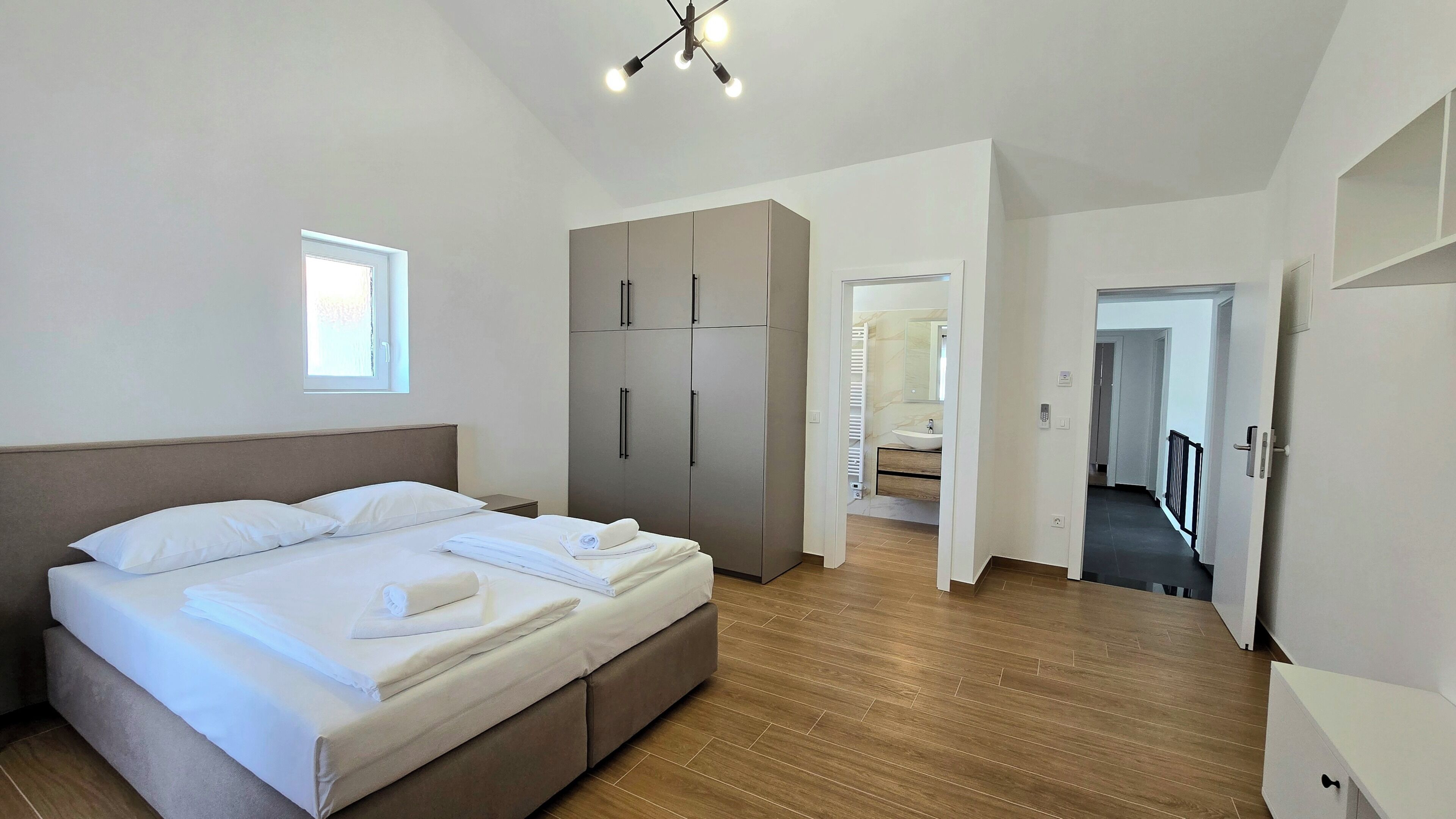 Ein modernes Schlafzimmer mit einem großen Bett, einem Kleiderschrank und einem durchgehenden Türrahmen einsehbarer Badezimmer.