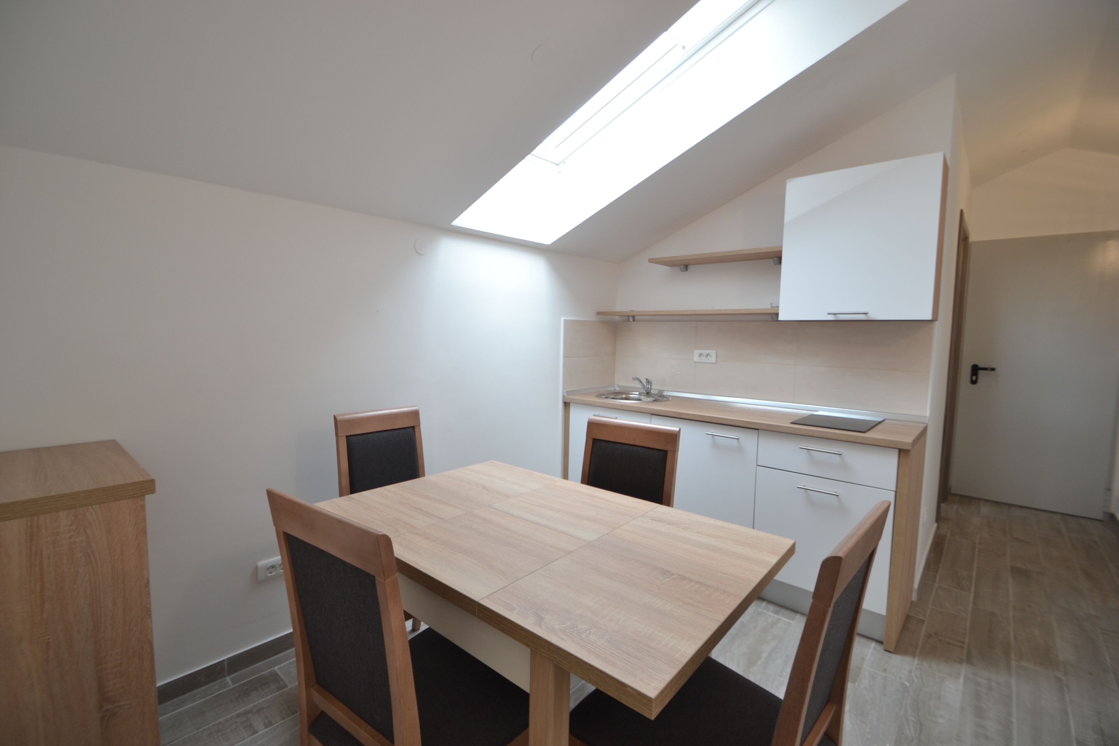 A compact kitchen with a skylight, a dining table with chairs, and a small cabinet.