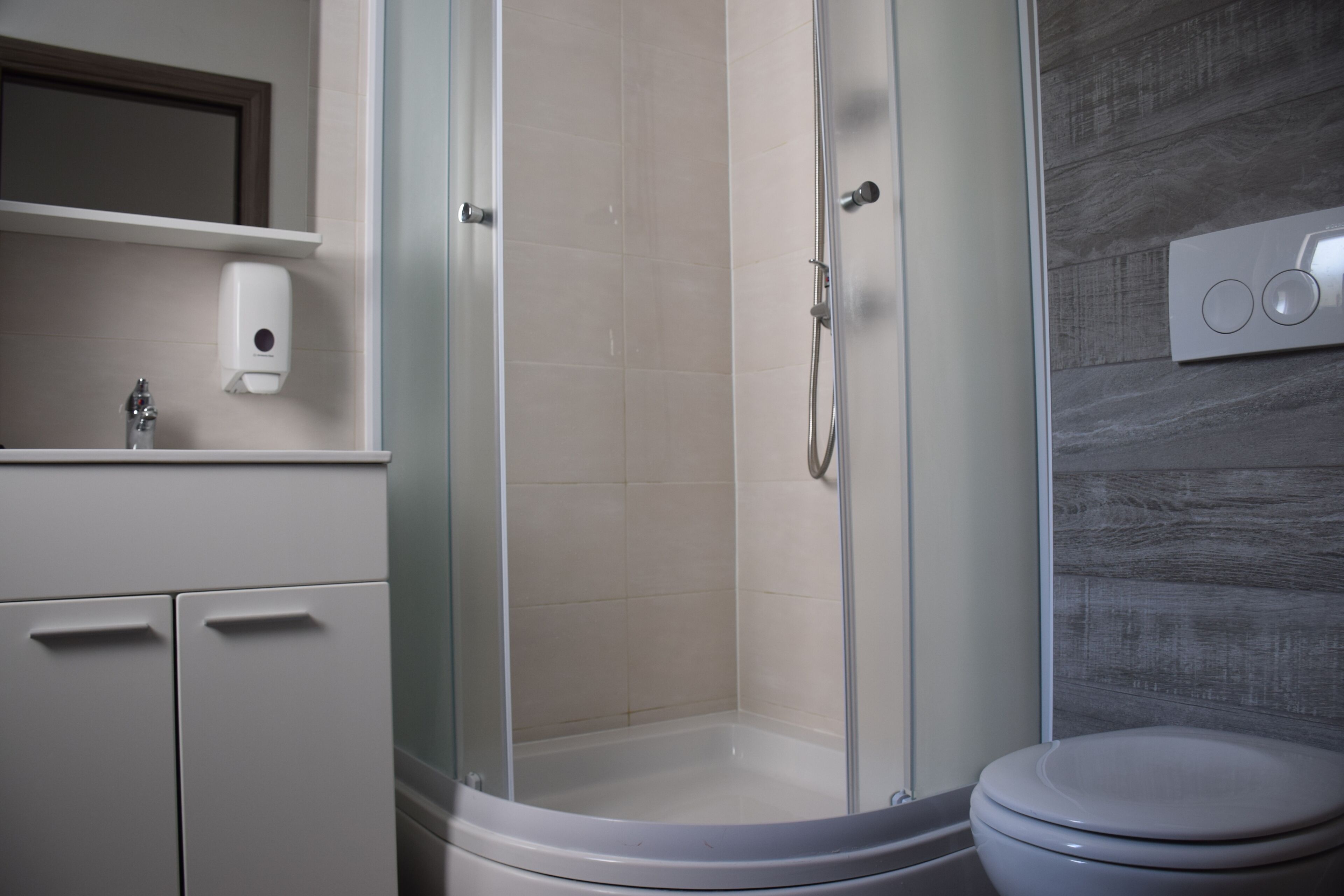 Een badkamer met een douche met glazen wand, een toilet en een zeepdispenser op een muur.