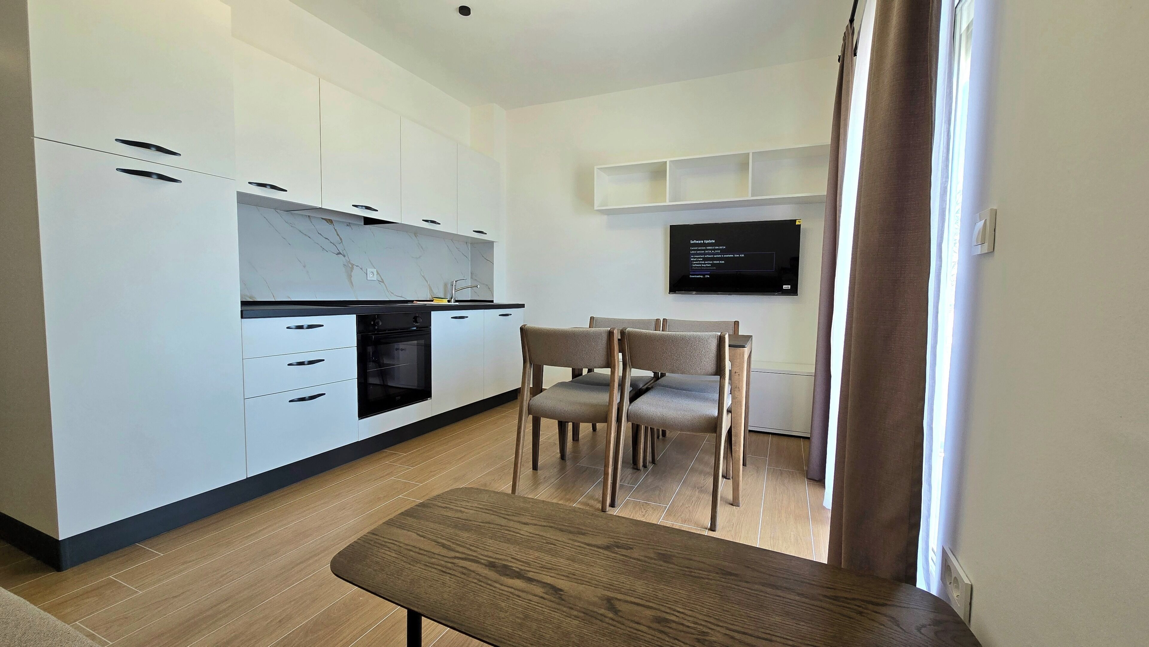 A modern kitchen with white cabinets, a built-in oven, and a dining area with a table and chairs.
