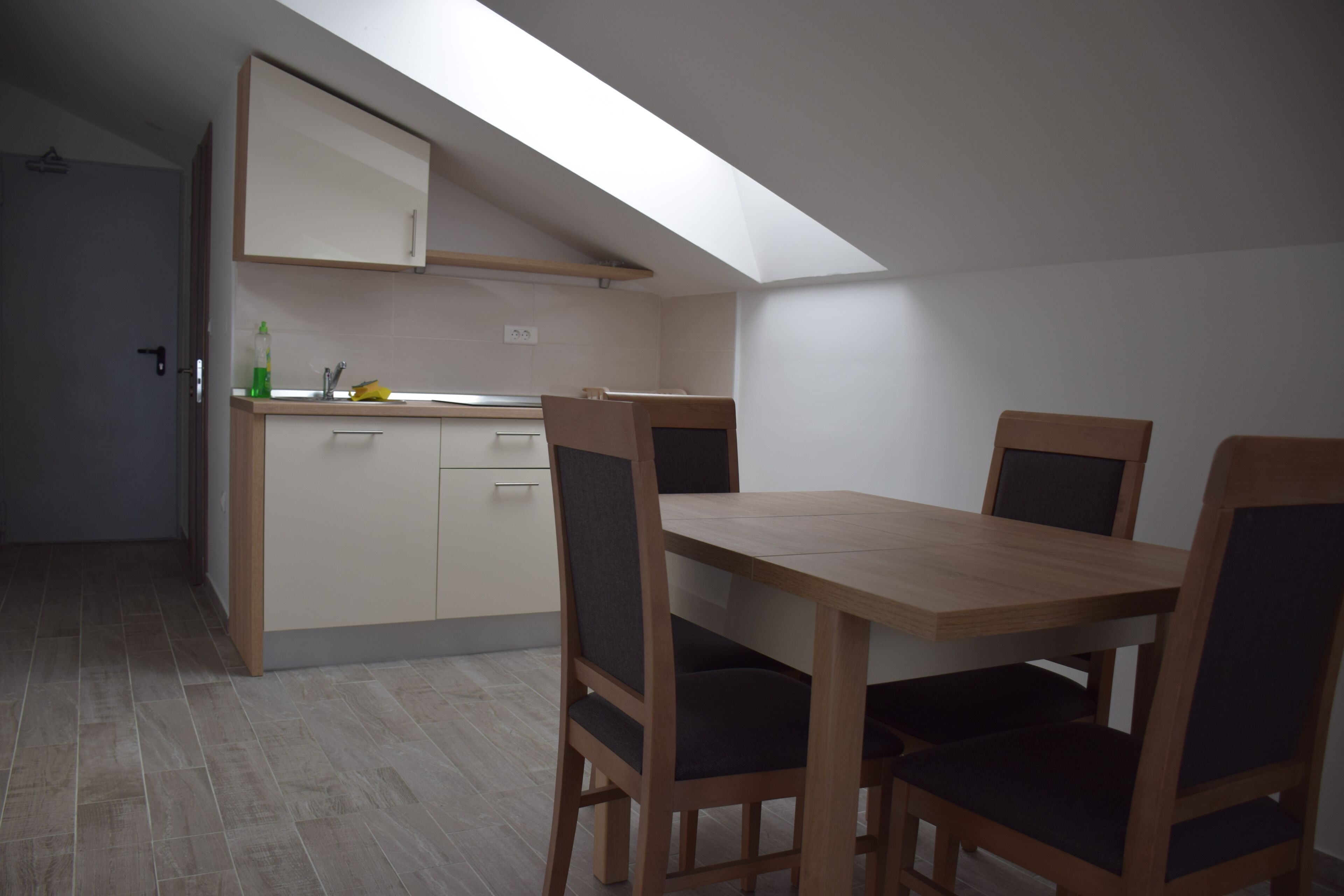 A compact kitchen with a dining area, a skylight, and a door leading to another room.