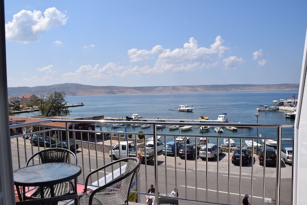 Un balcón con vistas a un puerto deportivo, barcos y un paisaje montañoso distante.