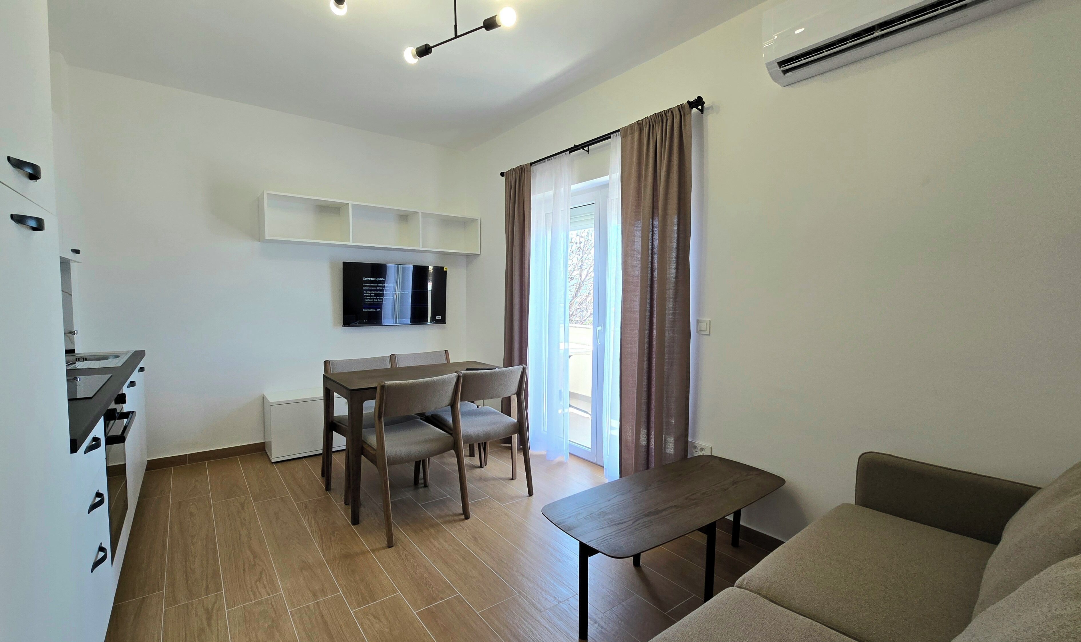 A modern living room with a sofa, a dining table with chairs, a TV mounted on the wall, and an air conditioning unit.