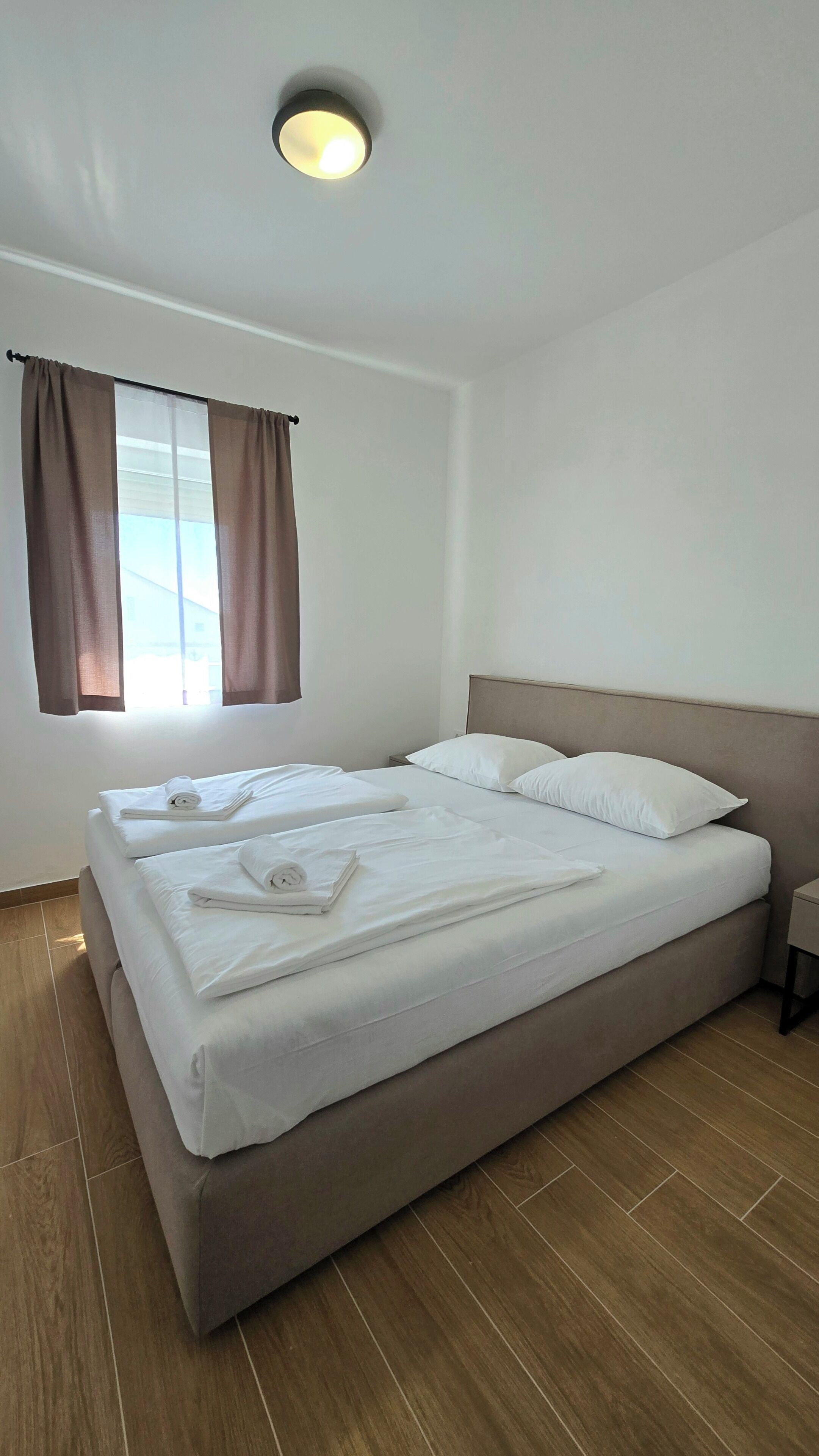Una habitación de hotel limpia y moderna con una cama grande, una mesita de noche y un ventanal con cortinas.