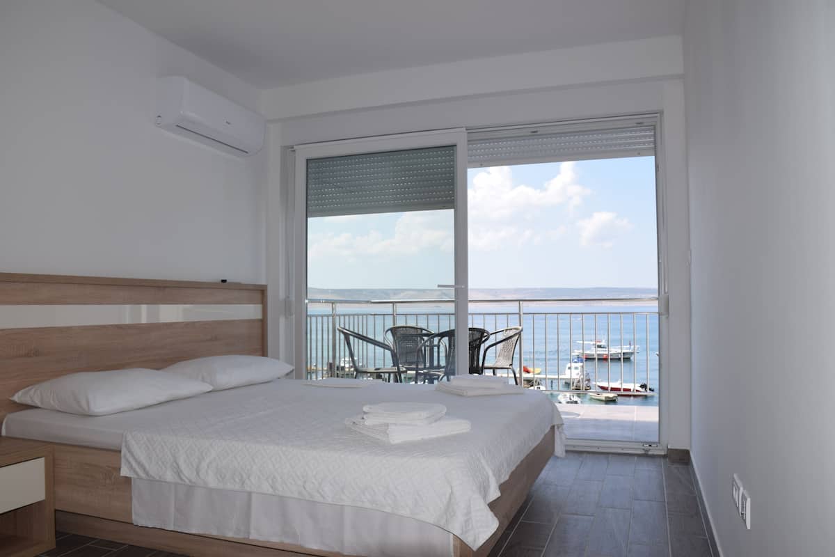 Une chambre à coucher comprenant un lit, une table de chevet, un balcon avec vue sur la mer et les bateaux, ainsi qu’une table avec des chaises.