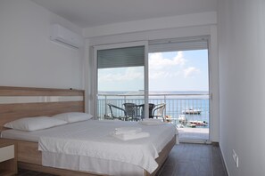 Un dormitorio con cama, mesita de noche, balcón con vistas al mar y barcos, y una mesa con sillas.