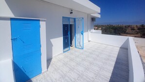 A modern building with white walls and blue doors, a flat roof, and a view of the landscape.