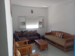 A living room with a sofa, a wooden chair, a small table, and two mirrors on the wall.