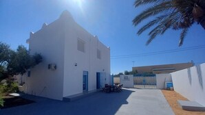 A white building with a blue door, a table with chairs, and a palm tree.