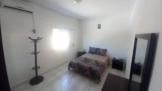 A bedroom with a bed, a bedside table, a nightstand, a wardrobe, a coat rack, and a ceiling fan.