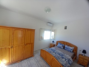 A bedroom with a wooden bed, a wardrobe, a bedside table, a nightstand, and a window.