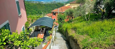 A narrow stone staircase leading to a covered outdoor seating area with a view of a hillside and distant mountains.