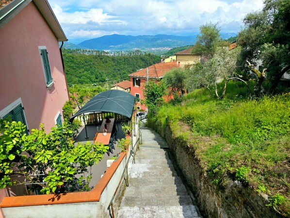 A narrow stone staircase leading to a covered outdoor seating area with a view of a hillside and distant mountains.
