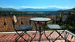En balkon med flisegulv, to metalstole, et rundt bord og udsigt til bjerge.