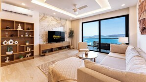 A modern living room with a flat-screen TV, wooden shelves, a sofa, and a large window overlooking the sea. - Stunning 2nd-Level | Views of Ocean, Beach & Pool (Huatulco)