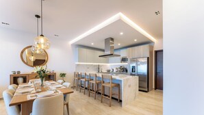A modern kitchen with a central island, bar stools, and a dining table set for six. - Stunning 2nd-Level | Views of Ocean, Beach & Pool (Huatulco)