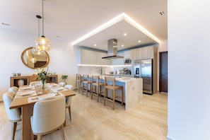 A modern kitchen with a central island, bar stools, and a dining table set for six. - Stunning 2nd-Level | Views of Ocean, Beach & Pool (Huatulco)