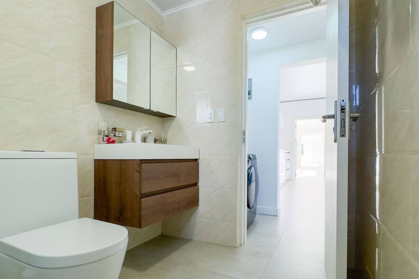 Une salle de bain comprenant des toilettes, un lavabo avec un miroir et une porte donnant sur une autre pièce.