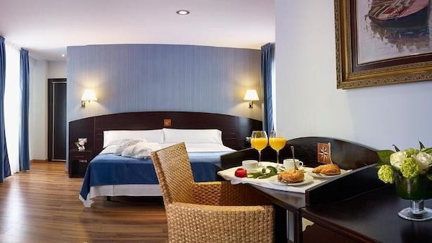 Una habitación de hotel con cama, una mesa de comedor con desayuno, una maleta y un radiador.