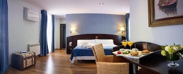 Una habitación de hotel con cama, una mesa de comedor con desayuno, una maleta y un radiador.