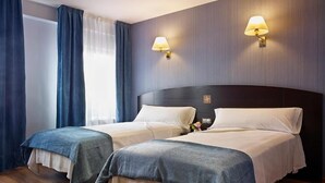 Habitación de hotel con dos camas, suelo de madera y dos lámparas fijadas a la pared.