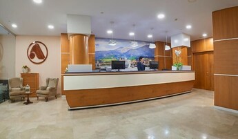 Zona de recepción de un hotel con un mostrador de madera, dos monitores de ordenador, un mural grande y un recepcionista detrás del mostrador.