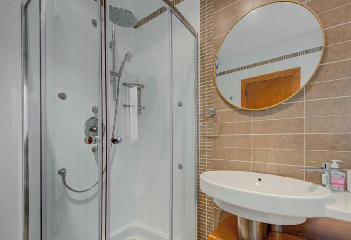 Une douche fermée par des parois en verre, dotée d’un pommeau de douche à main et d’un robinet mural.