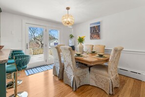 Ein Essbereich mit einem Holztisch, beigefarbenen Polsterstühlen, einer Chandelierleuchte und Blick durch die Glastür.