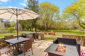An outdoor patio with a grill, dining table, chairs, and a fire pit.