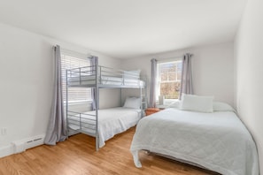 Ein Zimmer mit einem Etagenbett, einem Einzelbett und einem Fenster mit Vorhängen.