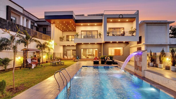 A modern building with a swimming pool, outdoor seating, and a waterfall feature. - ELIVAAS Horizon Luxe 5BHK Villa (Udaipur)