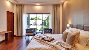 A hotel room with a large bed, a bench, a table with breakfast items, and a view of a garden and building outside. - ELIVAAS Horizon Luxe 5BHK Villa (Udaipur)