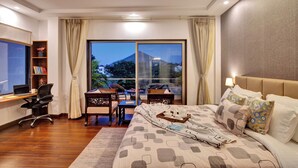 A hotel room with a bed, desk, chairs, and a large window with a view of a mountain. - ELIVAAS Horizon Luxe 5BHK Villa (Udaipur)