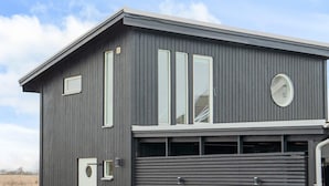 A modern building with a garage door, large windows, and a flat roof. - 4 Person Holiday Home in Tvaaker (Tvaaker)